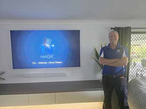 Technician standing by a wall mounting TV he installed.