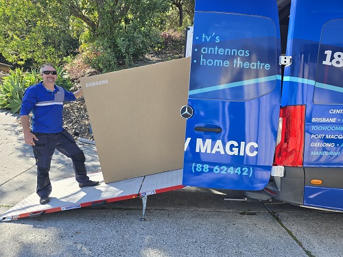 Technician loading a large TV into TV Magic van